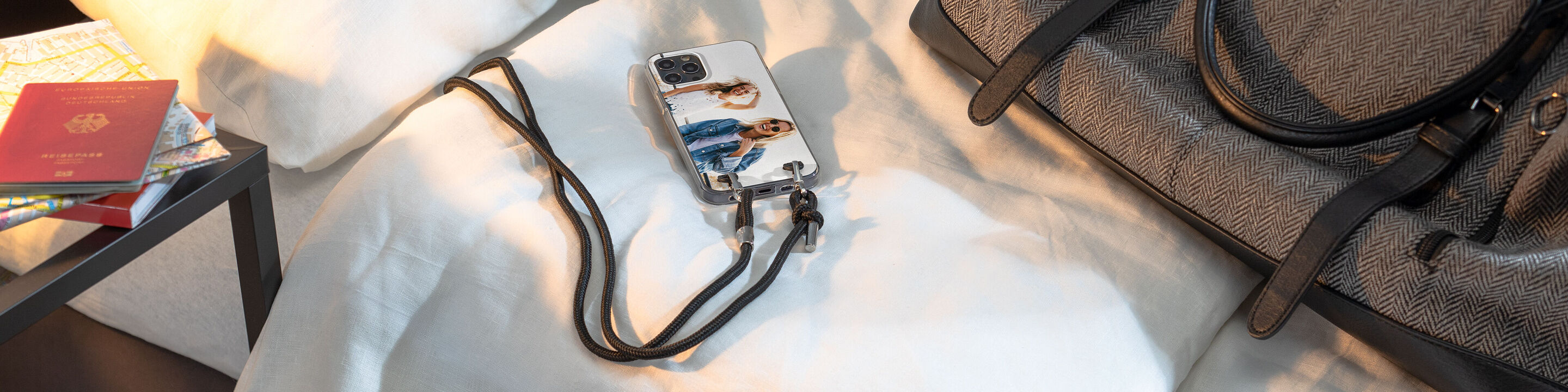 Un téléphone avec une coque personnalisée sur un lit à côté d'un sac et d'un passeport.