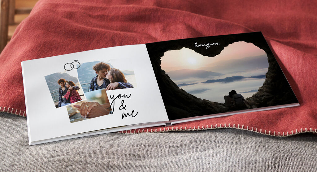 Un livre photo ouvert montre des moments romantiques d'un couple, entouré d'un paysage en forme de cœur. CEWE FOTOBOOK.