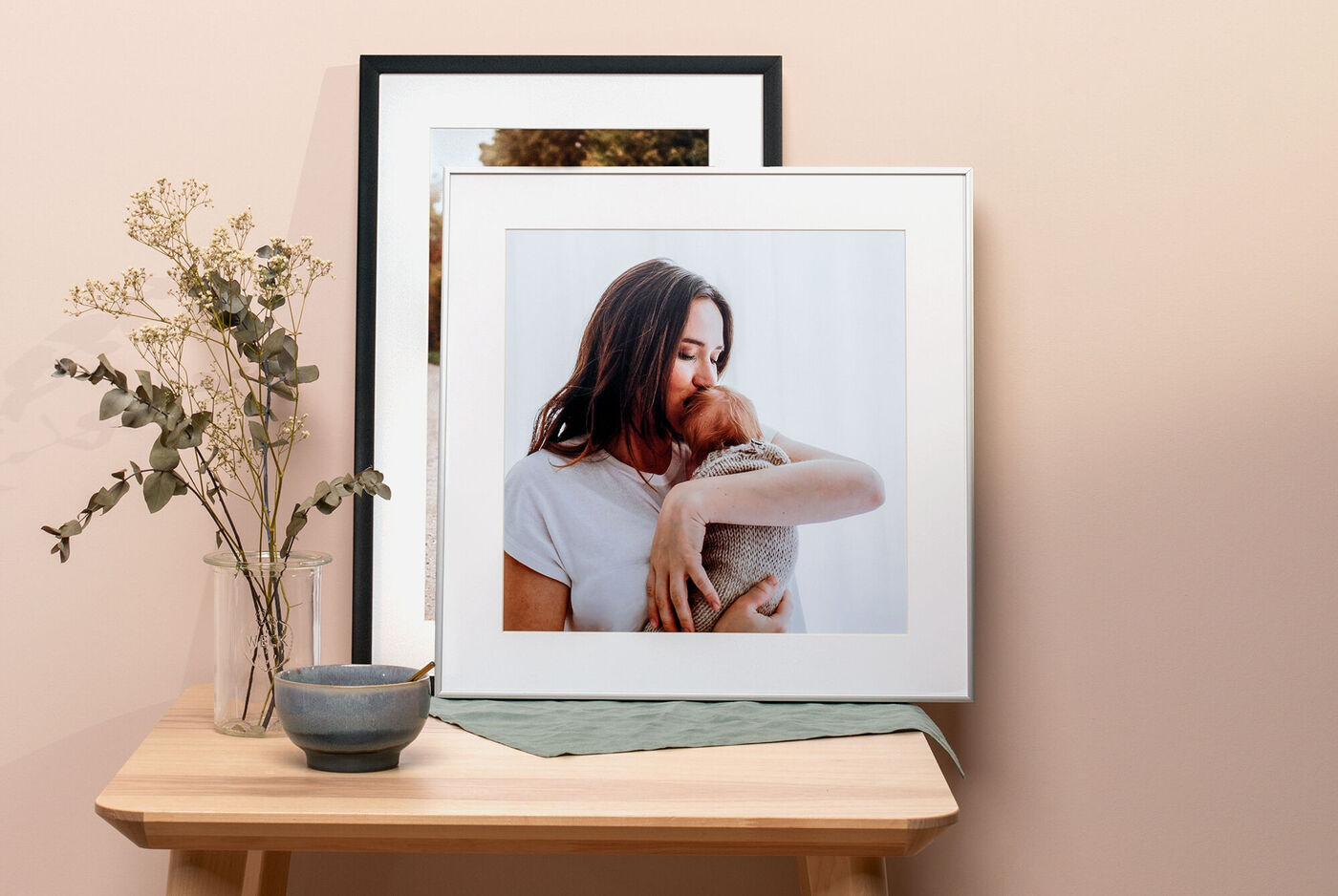 Photo encadrée d'une personne avec un animal de compagnie sur une table en bois, entourée d'un vase de fleurs.