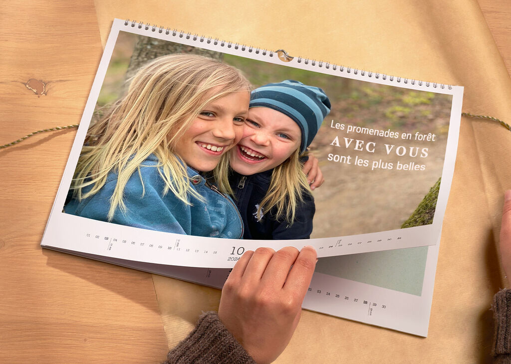 Un calendrier ouvert avec des photos d'enfants heureux souriants. La page montre le mois d'octobre et une belle scène forestière.