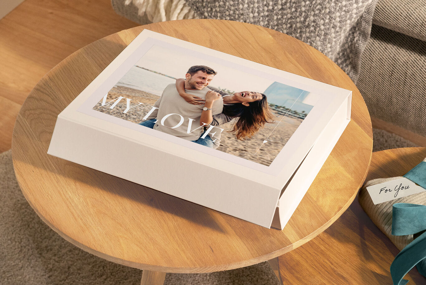 Un couple assis sur la plage rayonne de joie. La couverture de l'album CEWE affiche le mot 'MY LOVE'.