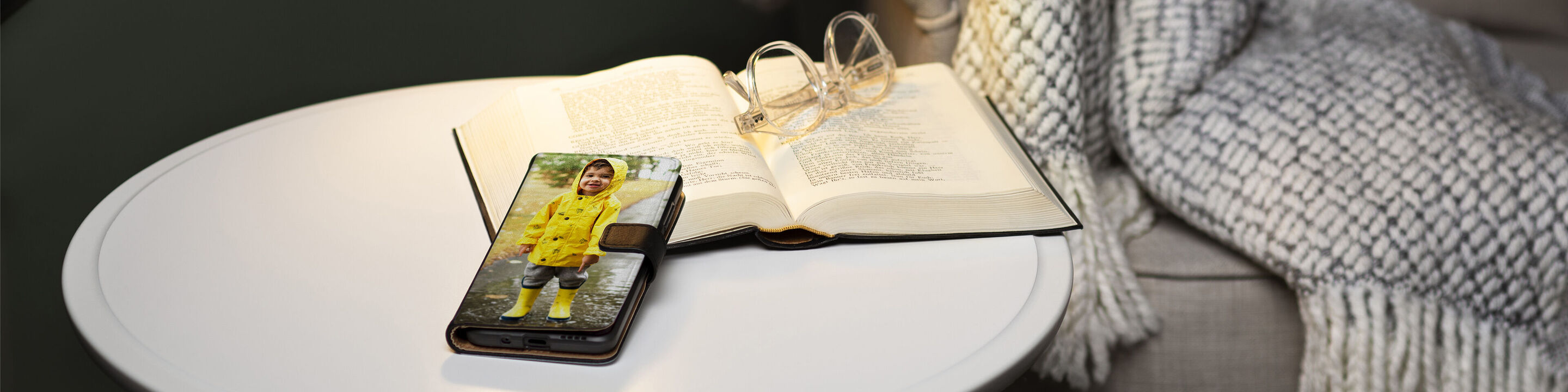 Un smartphone avec une image d'un enfant dans un manteau de pluie jaune sur une table, à côté d'un livre ouvert et de lunettes.