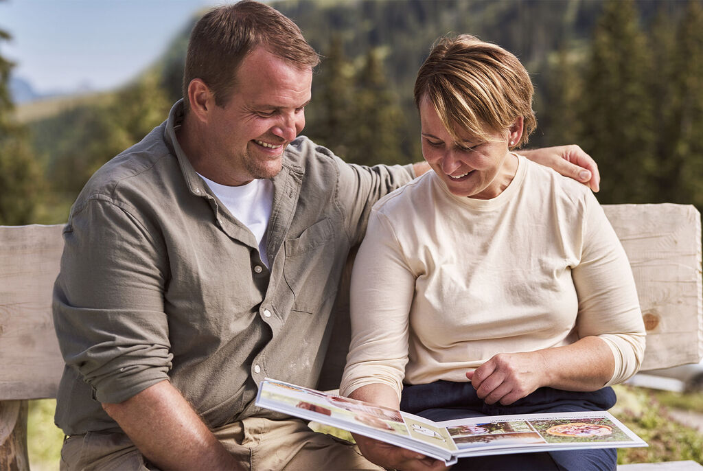 Un couple est assis sur un banc, regardant un album photo de leurs souvenirs en pleine nature.
