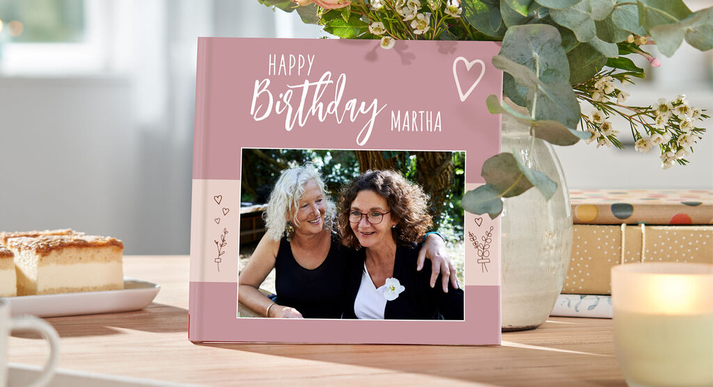 Deux amies fêtent un anniversaire avec un album photo à côté d'une belle disposition florale.