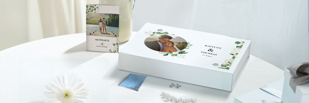 Un livre photo CEWE avec photo personnelle sur la couverture et des détails affectueux. Une fleur et une carte sont aussi sur la table.