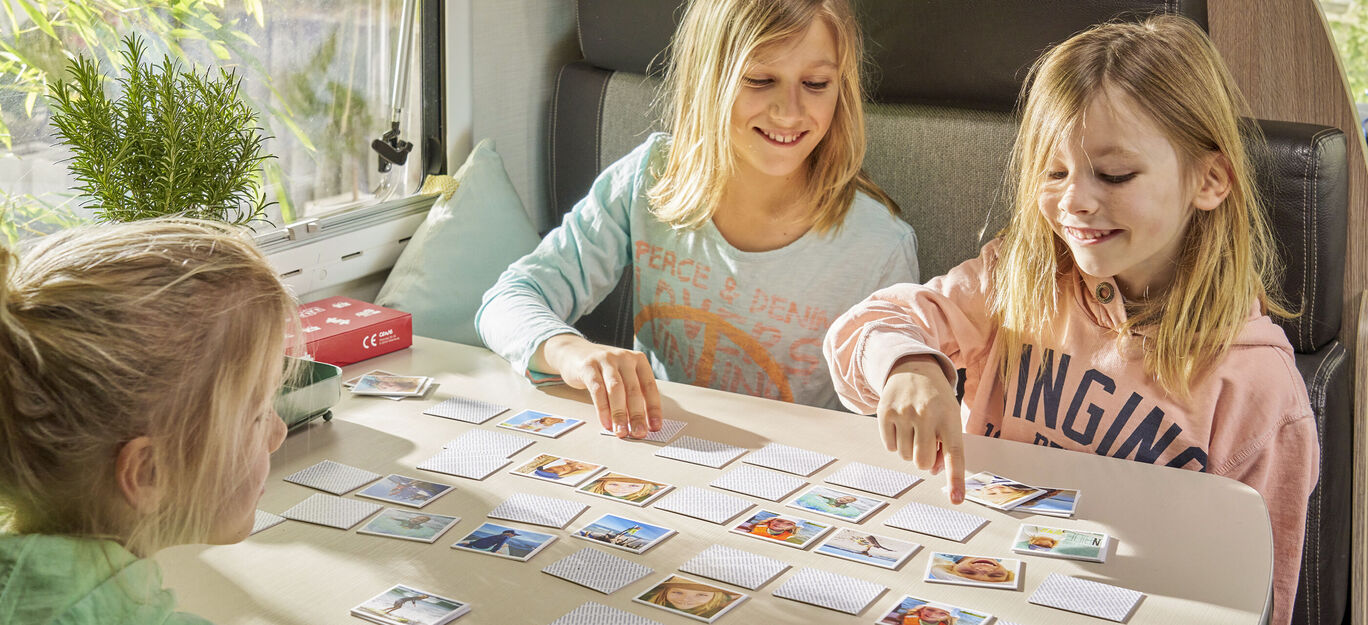 Trois enfants jouent à un jeu de mémoire avec de nombreuses cartes sur une table.