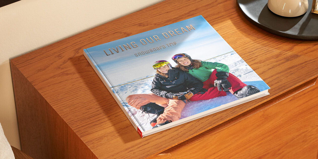 Un livre de photos fermé est posé sur une étagère en bois. Sur la couverture, on voit une photo de deux femmes dans la neige. Le titre « Living our Dream » est ennobli en lettres dorées.